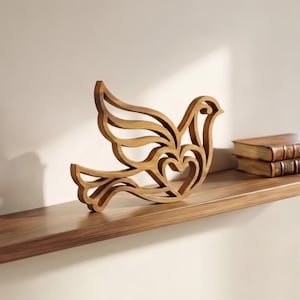 Könnte beinhalten: Eine hellbraune Holzschnitt-Skulptur in Form eines stilisierten Vogels im Flug. Das Design zeichnet sich durch durchbrochene Linien aus, die Flügel und Schwanz bilden, mit einem herzförmigen Ausschnitt in der Mitte des Vogelkörpers.