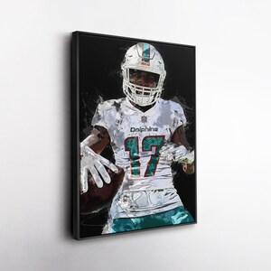 May include: A framed art print of an American football player in a white and teal uniform, holding a football. The player wears a helmet with a teal and orange stripe. The number 17 is visible on the jersey.
