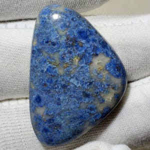 May include: A polished, triangular-shaped gemstone featuring a mottled pattern of deep blue, light blue, and creamy white mineral inclusions. The stone has a smooth, glossy surface with visible variations in color density and texture throughout.