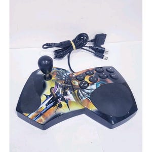 May include: A black video game controller with a joystick on the left side and a large circular button area on the right. The surface features a colorful graphic print of a fantasy creature. It includes a black wired cable with multiple connectors.
