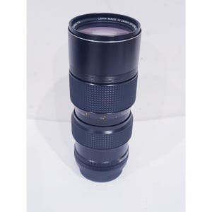 May include: A black camera lens with a textured grip ring and a smooth barrel. The front rim is inscribed with LENS MADE IN JAPAN. The lens features a focus ring with distance markings in feet and meters, and a zoom ring with 80-200mm markings.