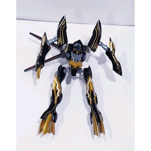 May include: A black and gold robot action figure with articulated limbs and wings. The figure has a detailed design with gold accents on the legs, arms, and chest. The robot's head is black with a silver faceplate. The figure is standing on a white surface.