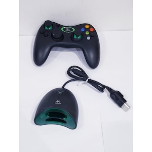 May include: Black Logitech gamepad with green accents and a matching base station. The controller has multiple colored buttons and analog sticks. The base station has a charging port and a power cord.