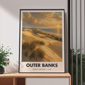 Pode incluir: Uma impressão de arte de parede vertical emoldurada apresentando um pôr do sol sobre os Outer Banks, Carolina do Norte, EUA. A imagem exibe dunas de areia dourada com manchas de grama de praia levando ao oceano sob um céu nublado. O texto diz OUTER BANKS NORTH CAROLINA USA.