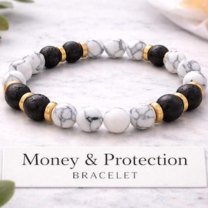 May include: A beaded bracelet featuring alternating black lava stone and white marble-like beads, separated by gold-colored spacers. The bracelet is displayed on a white surface, with the text "Money & Protection BRACELET" in a rectangular label.