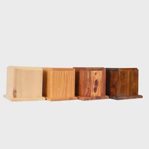 May include: Four wooden boxes of varying shades, from light to dark. The boxes are rectangular with a slightly curved top and a base. The wood grains and tones range from light tan to deep brown, showcasing natural wood variations.