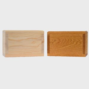May include: Two rectangular wooden boxes. One is light-colored, possibly pine, with visible wood grain. The other is a darker, reddish-brown, possibly oak, with a prominent wood grain pattern. Both boxes have a simple, clean design.