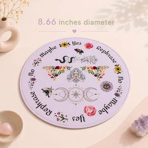 May include: A circular lavender mat with an 8.66 inches diameter, featuring printed text including Yes, No, Maybe, and Rephrase. The design includes illustrations of a central figure, a triple moon symbol, a snake, flowers, and moths.
