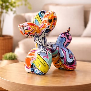 Peut inclure: Une sculpture de chien ballon colorée avec un design de style graffiti. La sculpture présente un mélange de teintes orange, jaune, bleu et rose, créant une esthétique ludique et artistique. Elle est posée sur une table ronde en bois.