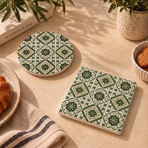 May include: Two drink coasters, one circular and one square, featuring a repeating geometric pattern in shades of dark green, olive, and cream. The design consists of stylized floral motifs enclosed within diamond and square borders on a white base.