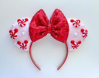 May include: Red and white candy cane themed Minnie Mouse ears with a red sequin bow. The ears are covered in white faux fur and have red and white candy cane embellishments.