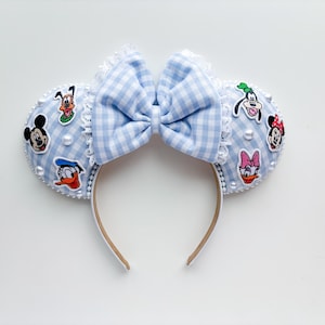 May include: Blue and white gingham Minnie Mouse ears headband with a bow and various Disney character patches including Mickey Mouse, Donald Duck, Goofy, and Pluto.