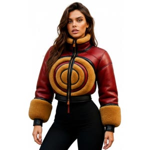 May include: A red leather jacket with a high collar and a circular design on the front. The jacket has tan-colored fur accents on the collar and cuffs, with a black zipper and trim. The jacket is cropped and has a fitted silhouette.