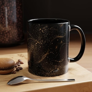 May include: A white ceramic mug with a black handle and the text "But First, Coffee" in a bold, black font. The mug is displayed on a white surface.