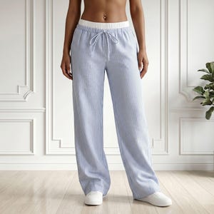 May include: Light blue and white pinstriped trousers featuring a wide-leg silhouette, a high-rise elastic waistband in solid white, and a matching drawstring tie at the center front. The pants are full-length and have a relaxed, loose fit.