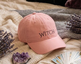 Peut inclure: Une casquette de baseball rose clair avec une visière incurvée et une calotte structurée. Le mot WITCH est brodé en lettres noires de style serif sur les panneaux avant. La casquette présente un bouton sur le dessus et des œillets cousus.
