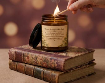 Peut inclure: Une bougie dans un pot en verre ambré avec un couvercle noir et une étiquette portant l'inscription Sweet Honeysuckle Spell, accompagnée d'un texte sur la bonne fortune. La bougie est allumée, dégageant une flamme et de la fumée.
