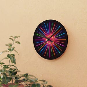 May include: A round black wall clock with a vibrant, colorful design. The clock face features a burst of neon-colored lines radiating from the center, creating a dynamic visual effect. The hands are black, and the clock is mounted on a beige wall.