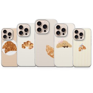 Può includere: Cinque custodie per telefono con disegni di croissant. Le custodie sono beige e bianco sporco, con illustrazioni di croissant, alcune con fiocchi. Progettate per uno smartphone.