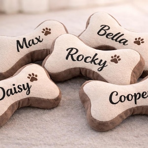 Può includere: Cinque giocattoli di peluche a forma di osso in color crema e marrone. Ogni giocattolo presenta un nome ricamato in marrone scuro: Max, Bella, Rocky, Daisy o Cooper, accompagnato da una piccola icona a forma di zampa. Il tessuto è morbido.