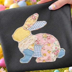 Pode incluir: Um tecido quadrado preto com um design de coelho de patchwork. O coelho é feito de vários tecidos, incluindo amarelo, rosa floral, xadrez azul e renda. A imagem é definida em um fundo de ovos de Páscoa e flores.