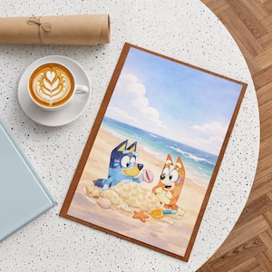 Puede incluir: Una impresión enmarcada que presenta dos perros de dibujos animados en una playa, con un cielo azul y un océano de fondo. Los perros interactúan con arena, conchas y una pala de juguete. La impresión tiene un borde marrón y está sobre una mesa blanca.