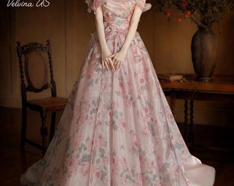 Könnte beinhalten: Ein rosa schulterfreies Kleid mit floralen Mustern und einem fließenden Rock. Das Kleid hat ein zartes Rosenmuster in Rosa und Grau. Der Text "Velvina US" ist im Bild sichtbar.