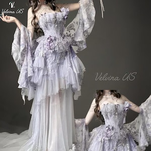 May include: A lavender corset dress featuring a strapless bodice with floral appliqués, layered tulle ruffles, and sheer flowing sleeves. The garment includes delicate chain accents and a long, multi-layered skirt with a sheer overlay. Text reads Velvina US.