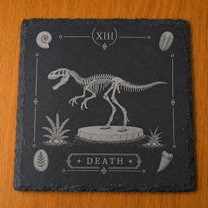 Puede incluir: Un posavasos cuadrado de pizarra negra con el grabado de un esqueleto de dinosaurio sobre una base circular. El dise&ntilde;o incluye el n&uacute;mero romano XIII en la parte superior, la palabra DEATH en la inferior y f&oacute;siles en las esquinas.
