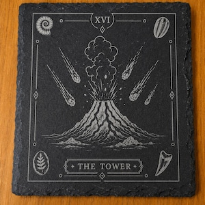 Puede incluir: Un posavasos cuadrado de pizarra negra con un grabado l&aacute;ser blanco de una erupci&oacute;n volc&aacute;nica y meteoritos. El dise&ntilde;o incluye el n&uacute;mero romano XVI, el texto THE TOWER e ilustraciones de f&oacute;siles en las esquinas del borde decorativo.