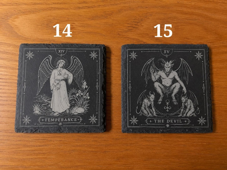 May include: Two square black slate coasters featuring white engraved tarot card designs. The left coaster, labeled 14, depicts Temperance with an angel. The right coaster, labeled 15, depicts The Devil with horned figures. Both have jagged edges.