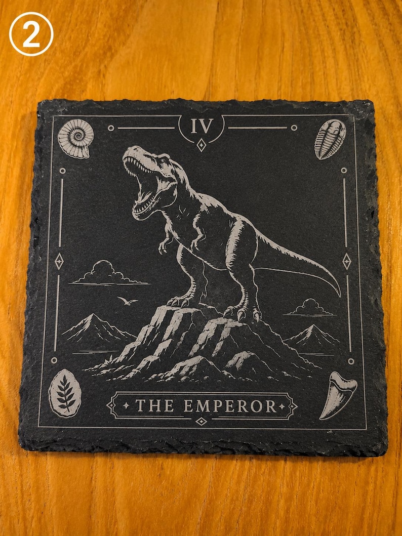 Puede incluir: Un posavasos cuadrado de pizarra negra con un grabado blanco de un Tyrannosaurus Rex sobre una cima monta&ntilde;osa. El dise&ntilde;o incluye el n&uacute;mero romano IV, el texto THE EMPEROR y peque&ntilde;os iconos de f&oacute;siles en las esquinas.