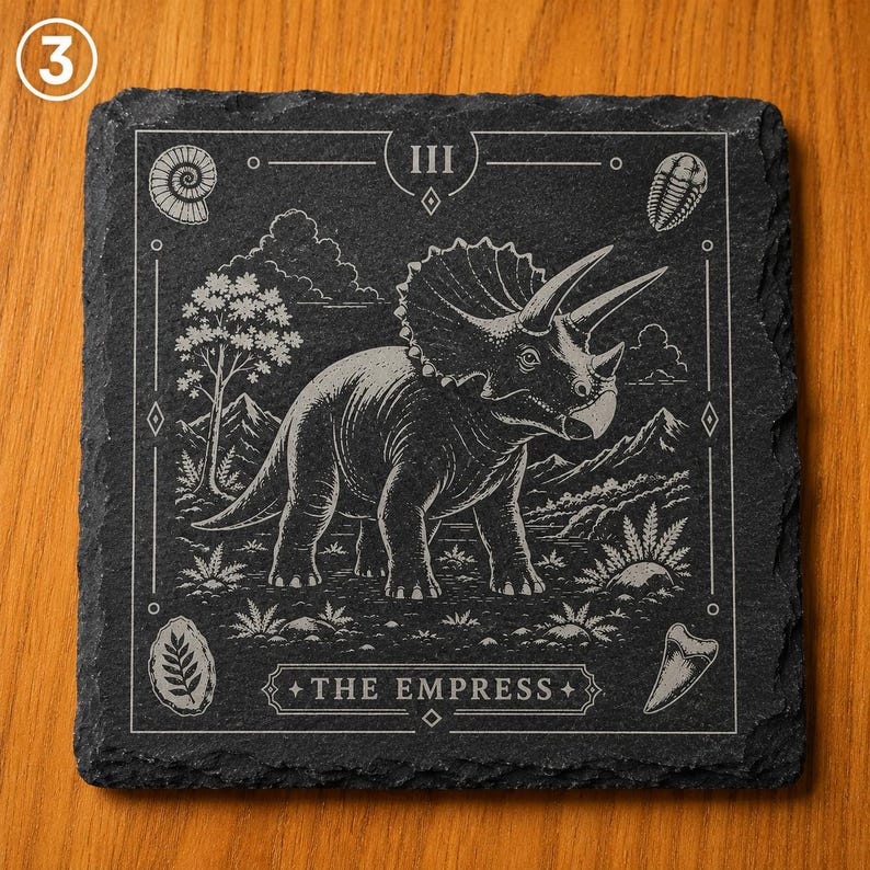 Puede incluir: Un posavasos cuadrado de pizarra negra con una ilustraci&oacute;n grabada a l&aacute;ser de un dinosaurio triceratops al estilo de una carta del tarot. El dise&ntilde;o incluye el n&uacute;mero romano III, el texto THE EMPRESS y varios f&oacute;siles prehist&oacute;ricos.