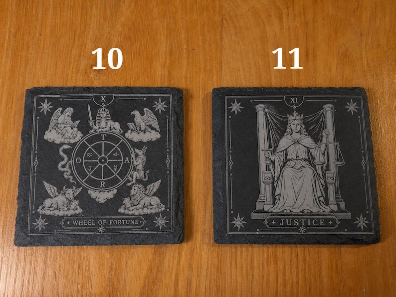 May include: Two square black slate coasters featuring engraved tarot card designs. The left coaster, labeled 10, depicts the Wheel of Fortune with celestial figures. The right coaster, labeled 11, shows the Justice card with a seated figure holding scales.