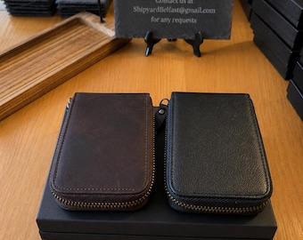 Könnte beinhalten: Zwei rechteckige Etuis mit Reißverschluss, eines in Dunkelbraun und eines in Schwarz, liegen auf einer schwarzen Schachtel. Ein Schieferschild dahinter zeigt SHIPYARD Local leathersmith and engraving und die E-Mail-Adresse ShipyardBelfast@gmail.com.