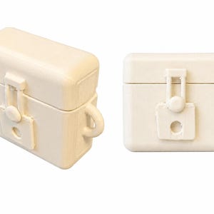 Könnte beinhalten: Cremefarbene, rechteckige Box mit Klappdeckel und Schnallenverschluss. Die Box hat einen kleinen Griff an der Seite und einen dekorativen Verschluss. Die Box besteht aus einem festen, undurchsichtigen Material.