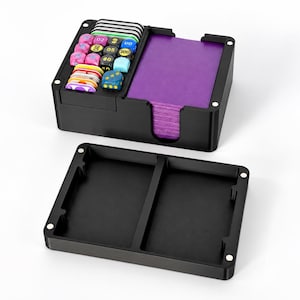 May include: A black rectangular game card storage box with a magnetic lid. The base contains a compartment filled with colorful dice and tokens, and a larger section holding a stack of purple cards. The lid is detached and placed in front.