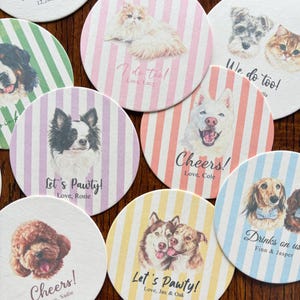 以下が含まれることがあります： 様々な犬種や猫種のイラストが描かれた丸いコースターのコレクション。各コースターにはパステルカラーのストライプの背景、ペットの肖像画、Cheers、Let's Pawty、We do tooなどのテキストが印刷されています。