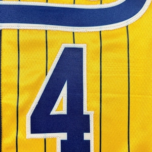 May include: A yellow athletic jersey featuring thin vertical black pinstripes and the large number 4 in dark blue with a white border. The upper portion displays a partial dark blue script logo with a white outline, all rendered in fabric.