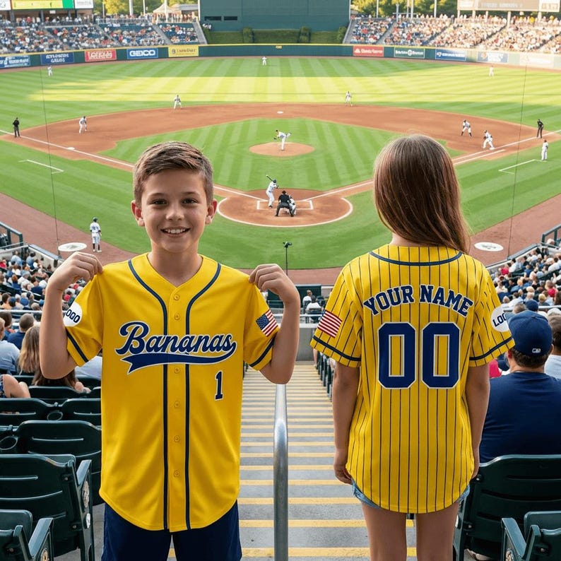 May include: A yellow baseball jersey with blue pinstripes, blue trim, and the text Bananas on the front with the number 1. The back features the text YOUR NAME and the number 00, with an American flag patch on the sleeve and a logo on the side.