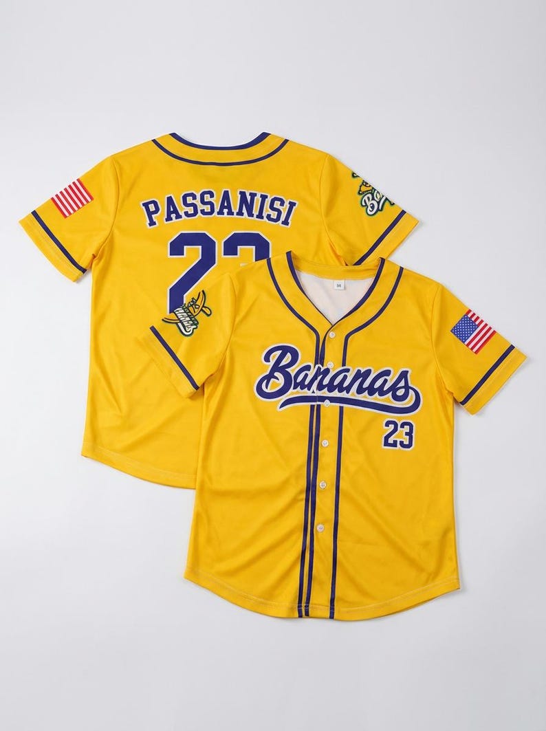 May include: A yellow baseball jersey with purple trim, featuring the text Bananas and the number 23 on the front. The back displays the name Passanisi and the number 23. Both sleeves feature a small American flag patch and a graphic logo.