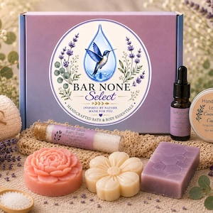 May include: A bath and body gift set featuring a purple box with a hummingbird logo, a glass vial of Wild Sage bath salts, a small dropper bottle, a round tin of cocoa butter lotion, a pink flower soap, a cream flower soap, and a purple bar soap.