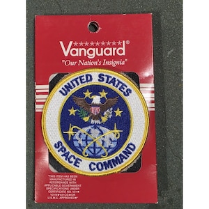 May include: A circular patch featuring the words "UNITED STATES SPACE COMMAND" in white lettering on a blue background. The patch includes an eagle emblem and stars. The patch is on a red card with the Vanguard logo.