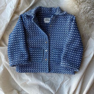 May include: A blue and white patterned jacket with a collared neckline and three gold buttons. The jacket has a square pattern and a small pocket. The label reads "Dear Vanessa".