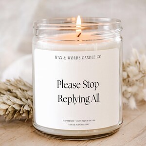 以下が含まれることがあります： 白いラベルが付いた、火の灯った透明なガラス瓶キャンドル。ラベルには黒い文字で「Please Stop Replying All」と書かれています。キャンドルはWax & Words Candle Co.のもので、環境に優しく、ビーガンで、米国製です。