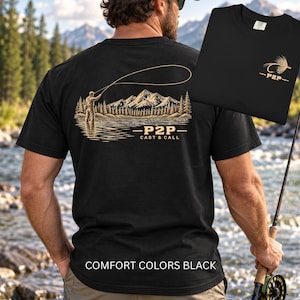 May include: A black short-sleeve t-shirt featuring a tan graphic on the back of a person fly fishing in a lake with mountains and trees. The text P2P CAST & CALL is printed below the scene. A smaller matching graphic is on the front chest area.
