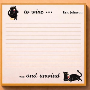 May include: A notepad with a cream-colored background and a gold border. The notepad has horizontal lines for writing and features illustrations of black cats with wine glasses. Text on the notepad reads "to wine ... and unwind" and "Eric Johnson."