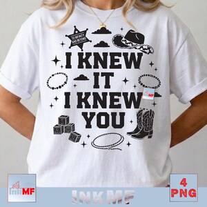 May include: A white short-sleeved t-shirt featuring a black graphic print with the text I KNEW IT I KNEW YOU. The design includes a sheriff star, cowboy hat, cowboy boots, alphabet blocks, a lasso, clouds, and stars scattered around the text.