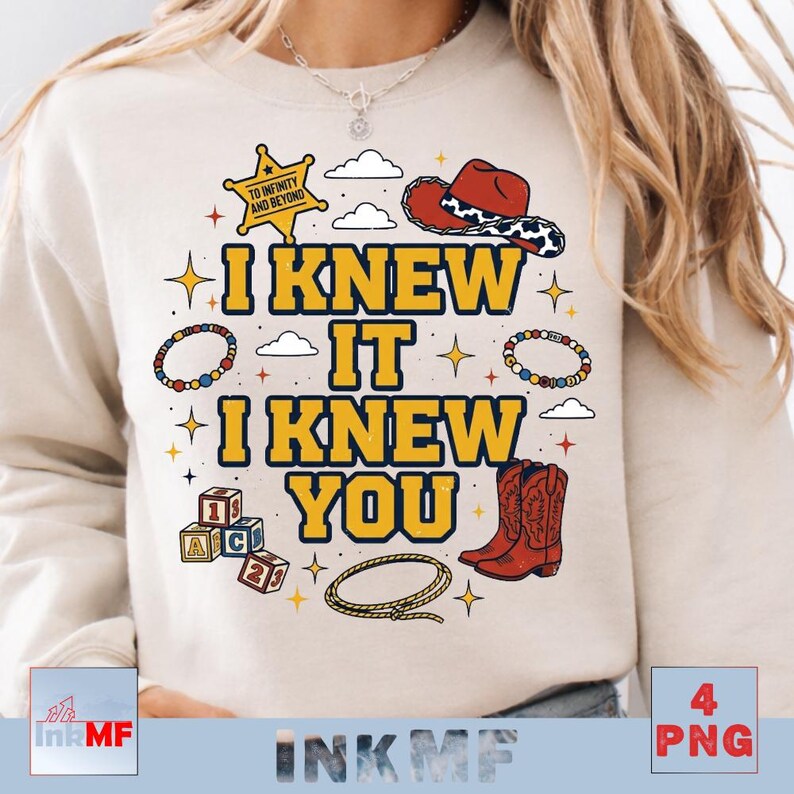 May include: A beige crewneck sweatshirt featuring a graphic print with the text I KNEW IT I KNEW YOU in yellow with blue outlines. The design includes a yellow sheriff star, a red cowboy hat, alphabet blocks, a lasso, and colorful beaded bracelets.