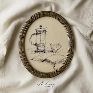 May include: An oval framed pen and ink drawing depicts a coffee press, cup, and open book. The artwork is in a gold-colored ornate frame. The words "Archive Art Co." are at the bottom of the frame.